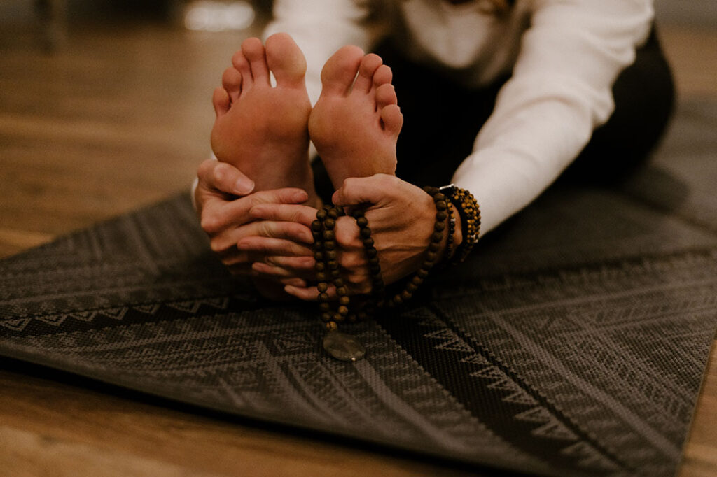 Seated person locking fingers around their feet in a stretching pose on a mat